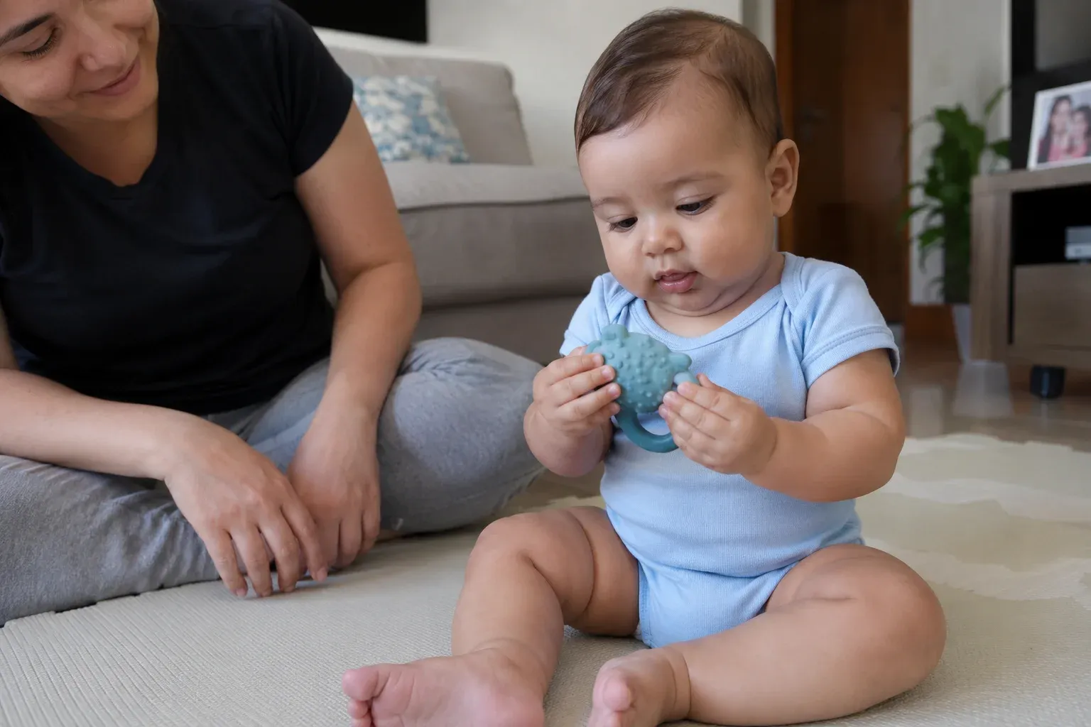 Bebê explorando com as mãos o relevo de um mordedor, com um adulto próximo.