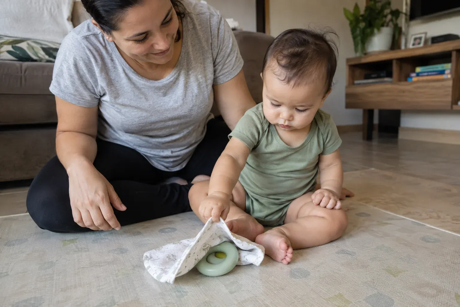 Bebê levantando a borda de um pano para encontrar um brinquedo parcialmente escondido.